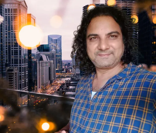 Nishad Raj Rana, smiling, in a checked shirt against a city skyline at dusk